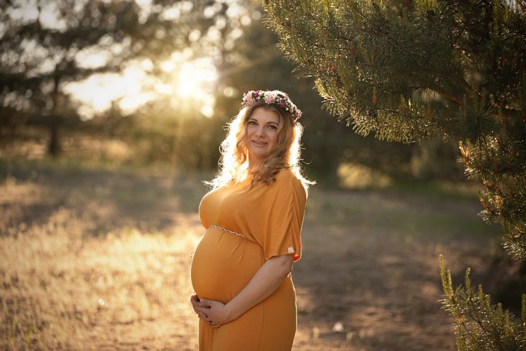 Das Bild zeigt eine schwangere Frau im orangefarbenen Kleid bei einem Outdoor Babybauch Shooting im Park.