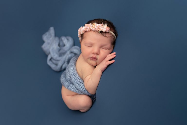 Das Bild zeigt ein schlafendes Neugeborenes mit Blumenhaarkranz auf einer blauen Decke wunderschöne Babyfotografie von Sanja Balceva, Babyfotografin für Mannheim, Heidelberg, Darmstadt und Umgebung