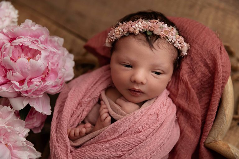 Das Bild zeigt ein Neugeborenes Baby mit rosefarbenem Blumenhaarkranz in wunderschöner Newborn-Pose - geshootet bei einem Baby-Fotoshooting von Sanja Balceva, Babyfotografin für Mannheim, Heidelberg, Darmstadt und Umgebung