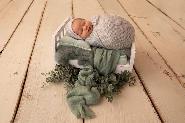 Neugeborenes Baby liegt eingepuckt auf Bettchen auf mintgrünen Tüchern und Eykalyptus – wunderschönes Foto aufgenommen beim Neugeborenen-Shooting im Studio in Birkenau Nähe Mannheim, Heidelberg und Darmstadt