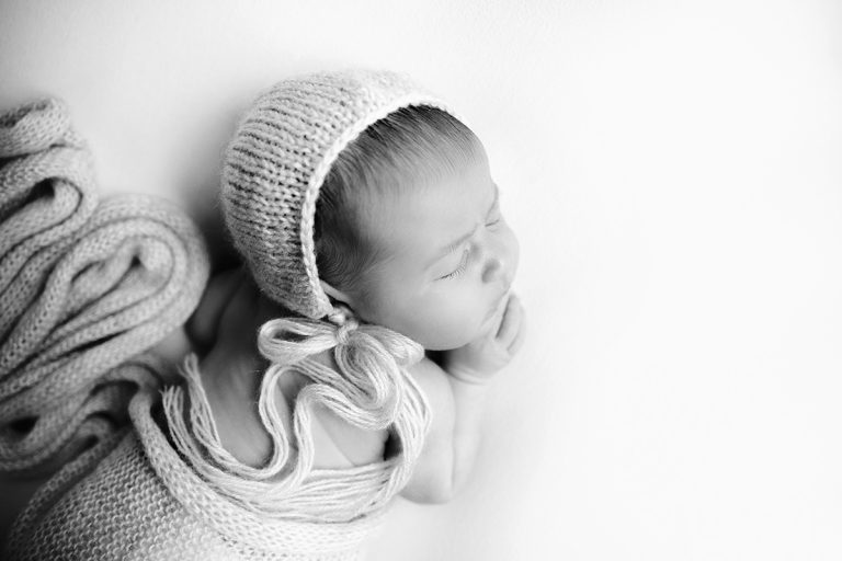Neugeborenes Baby liegt auf weißem Tuch auf dem Bauch und trägt ein Mützchen - Sanja Balceva - deine Fotografin für traumhafte Neugeborenenfotos in Mannheim, Heidelberg, Darmstadt und Umgebung