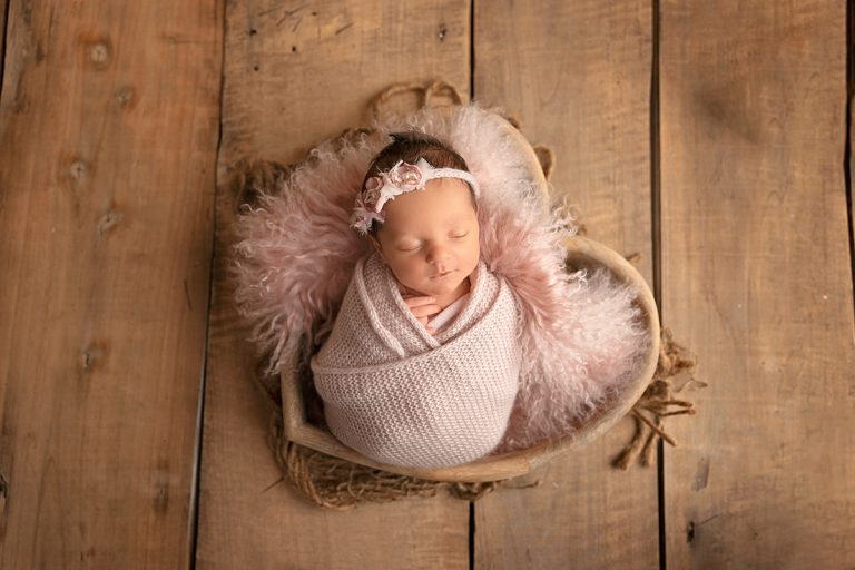 Neugeborenes Baby liegt beim Newborn Fotoshooting in Birkenau bei Heidelberg eingepuckt in Herzschale auf dunklem Holzhintergrund