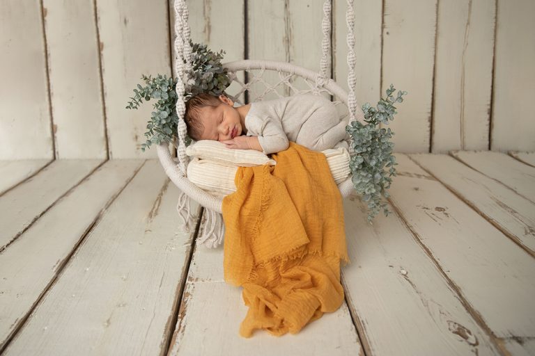 Neugeborener Baby Junge liegt in einem beigen Strampler auf einer Macramee Schaukel – wunderschönes Foto entstanden beim Neugeborenen-Fotoshooting im Studio bei Mannheim